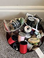 Top view of bowl filled with thread spools, bobbins, elastic, scissors tin