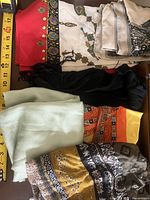 Stack of six folded scarves showing variety of colors and patterns with tape measure for scale