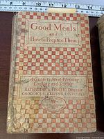 Front cover of Good Meals and How to Prepare Them showing checkered cloth design and worn spine