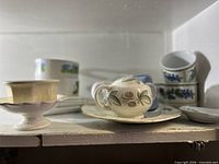 Shelf view showing sugar bowl on plate, dessert bowl, stacked cups, spoon rest