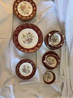 Stacked plates, saucers and soup bowls displaying floral centres and burgundy gilt rims