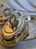 Two oval silver-plated covered dishes with finial handles shown together