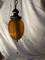 Full view of amber ribbed glass pendant light with brass cap and pull chain