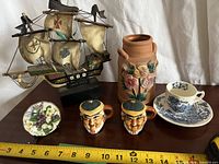 Group shot of all seven items including model ship, plate, creamers, cup, saucer, terracotta vase with measuring tape for scale