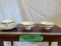 Stack of saucers and two of three handled soup bowls on table with ruler