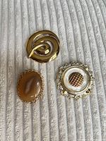 Front view of all three brooches showing design, materials and colours