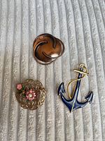 Front view of three brooches: copper swirl, filigree floral, blue anchor