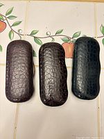 Three cases closed, showing crocodile-embossed exteriors in brown, dark brown and green