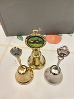 Front view of three souvenir bells showing materials and enamel crests