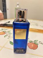 Front view of blue glass fragrance mist bottle with cap and label visible