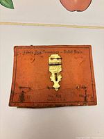 Front of latch on orange card showing model and material