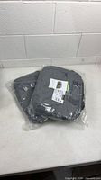 Two sealed grey Lenovo laptop bags on table
