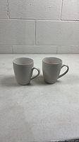 Front view of two off-white textured mugs