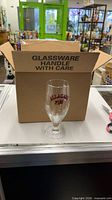 Open shipping box showing Allagash glass and outer carton marked "Glassware Handle with Care"