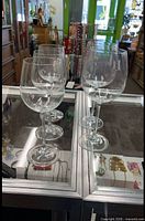Five clear stemmed wine glasses on glass display; shows 3 white and 2 red versions