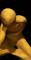 Close-up of gold abstract seated figure sculpture showing head resting on hand and textured finish