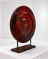 Three-quarter side view showing spiral form, red finish, copper patina, twin rod supports and textured base