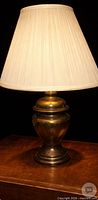 Full view of brass lamp on table with shade illuminated