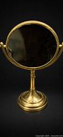 Front view of circular brass vanity mirror on pedestal stand