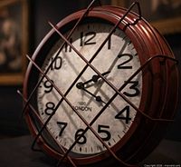 Angled view of red metal wall clock with wire cage showing dial and hands