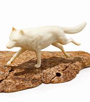 Profile view of ivory-toned wolf figure mounted on burlwood base