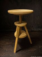 Full view of adjustable wooden tripod stool showing circular seat, screw column, lower disc, and three legs