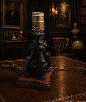 Front view of ornate black table lamp base with wood plinth and brass socket