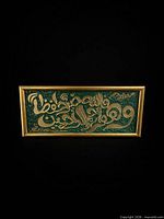 Front view of rectangular green and gold Arabic calligraphy plaque in gold frame