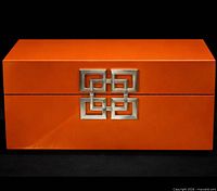 Front view of orange lacquer box showing metal geometric ornament