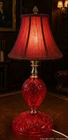 Full view of ruby red cut glass lamp showing base, body, and brass hardware