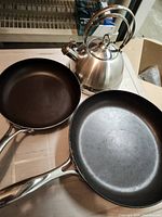 Top view of two non-stick frying pans and stainless tea kettle