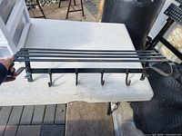 Full view of black metal coat rack showing hooks and slat shelf