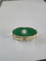 Closed pill box top view showing green enamel lid with white starburst and gold-tone rim