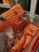 Plastic tote containing multiple orange bubble-wrapped glass vases with packing peanuts