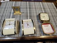 Group shot showing four clocks: two white Concord barrel alarms, one Fisher folding travel alarm, one Westclox miniature desk clock