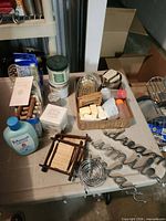 Overall lot view on table showing Johnson's bottle, basket with soaps, metal wall words, bamboo coaster, metal spiral, assorted containers