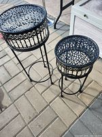 Two ornate black wrought iron plant stands different heights