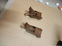 Top view of both rusted bear head coat hooks on cardboard