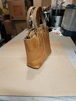 Side view of small brown leather Roots handbag showing handles and stitching