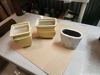 Two yellow square ceramic planters and one white oval concrete planter on tabletop