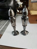Front view of both tall silver-plate shakers showing ornate pattern and patina