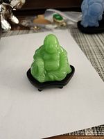 Front view of green glass Laughing Buddha on black stand