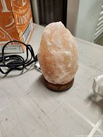 Front view of small pink Himalayan salt lamp on wood base with cord visible