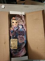 Doll in original box showing purple dress, hang tag, parasol