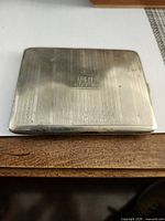 Front of silver-plated cigarette case showing monogram and striped guilloche pattern
