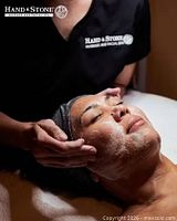 therapist performing facial treatment on client, Hand & Stone logo visible