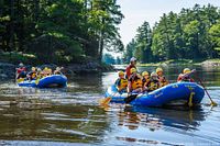 Two blue Wilderness Tours rafts with participants paddling on calm river
