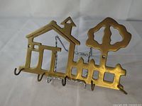Front view showing brass house, tree, fence silhouette and four hooks