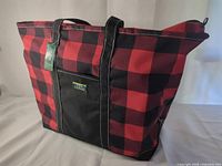 Overall view of tote showing plaid pattern, black front panel, handles, hang tag