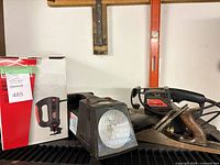 Lot overview showing boxed jigsaw, floodlight, Craftsman belt sander and hand plane